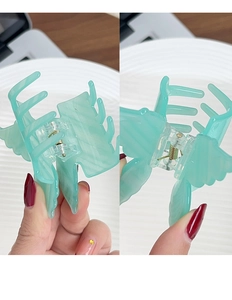 Detail of mint green acrylic butterfly hair claw clip with marble texture and gold spring