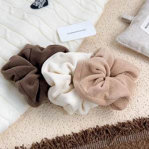 Three soft fleece scrunchies in brown, cream, and tan on a warm winter background