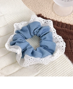 Detail of light blue fabric scrunchie with white eyelet lace trim on knitted background