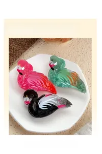 Close-up of three colorful flamingo-shaped acrylic hair claw clips in a decorative tray