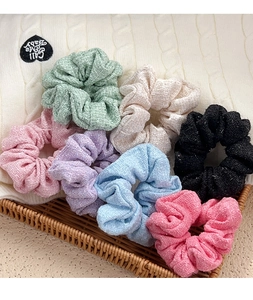 Set of seven multi-colored tweed scrunchies in a woven basket on a soft knit background
