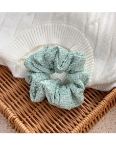 Detail of light green tweed scrunchie on woven tray with soft focus aesthetic
