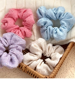 Set of four tweed scrunchies in pastel pink, blue, purple and beige on knit fabric