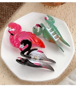 Detailed close-up of flamingo-shaped hair claws in pink, green, and black acrylic finish