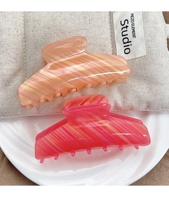 Detail view of peach and rose pink marble patterned acrylic hair claws in a set of two