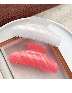 Detail view of pearlescent white and pink striped acetate hair claws in a wooden box
