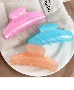 Three marble-textured hair claws in pink, blue, and orange on a minimalist ceramic plate