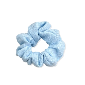 Minimalist light blue tweed fabric scrunchie with textured weave on white background
