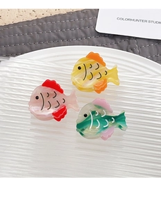 Close-up of three colorful acetate fish-shaped hair clips in yellow, pink, and green