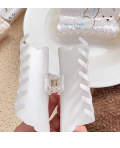 Detail of white wavy-edged acrylic hair claw clip with golden metal spring and teeth