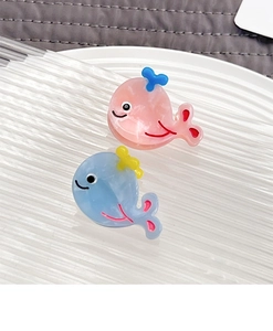 Close-up of pink and blue whale-shaped acetate hair clips on a white striped tray
