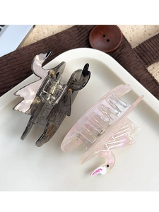 Detail view of two swan-shaped acetate hair claws in dark tortoise and pearly pink finishes