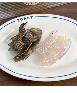 Detail view of two swan-shaped hair clips in dark tortoiseshell and pearly pink finish
