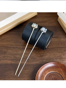 Close-up of two elegant lotus flower hairpins in silver and light gold on a dark wooden desk