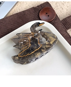 Detailed close-up of swan-shaped acetate hair claw with gold trim on a ceramic tray