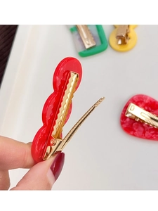 Detail showing the golden metal clip mechanism on red acrylic wavy duckbill hair clip