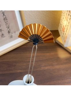Detail view of golden fan-shaped hairpin with textured folds and classic black accents