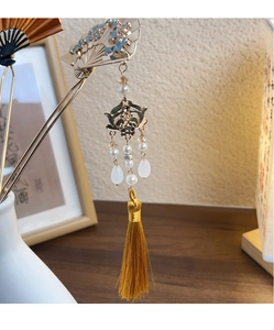 Detailed close-up of a vintage golden hair fork with blue flowers and yellow silk tassels