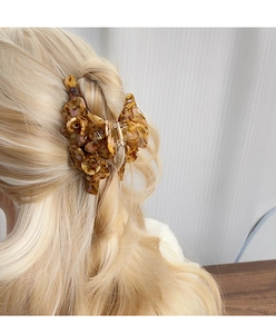 Gros plan d'une grande pince à cheveux fleur en acétate ambré portée par un modèle