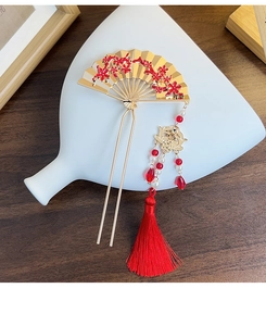 Close-up of golden fan-shaped hair fork with red plum blossoms and silk tassel