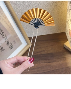 Detailed close-up of a golden fan-shaped hair fork with black ribs and dual-prong U-shape design