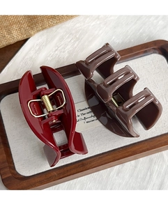 Close-up of deep red and brown glossy hair claws with strong gold metal springs in a tray