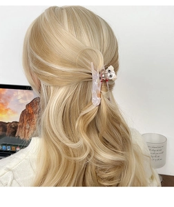 Détail d'une pince à cheveux en résine marbrée rose avec un ourson sur cheveux blonds