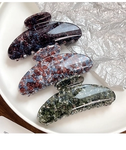 Detailed view of three marble texture acetate hair claws in purple, blue, and green finishes