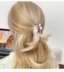 Gros plan d'une pince à cheveux en marbre rose portée sur des cheveux blonds bouclés