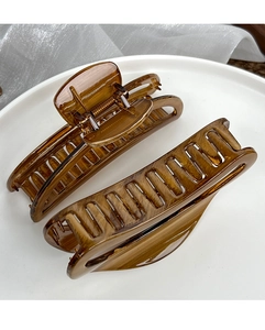Detailed view of amber wood-grain hair claw clips with hollow design on white tray