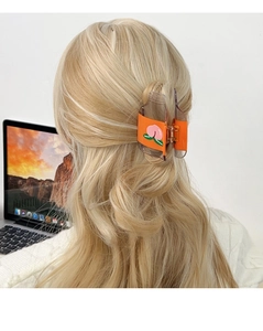 Pince à cheveux orange translucide avec motif pêche sur cheveux blonds vue de l'arrière