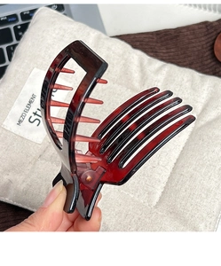 Détail d'une pince à cheveux à motif écaille de tortue rouge foncé tenue à la main