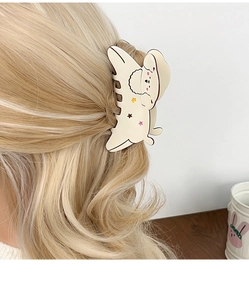 Detail showing creamy white dog hair claw clip with colorful stars on blonde curly hair
