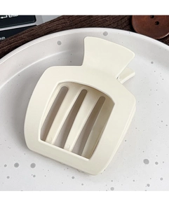 Détail d'une pince à cheveux mate crème avec découpes verticales sur une assiette en porcelaine