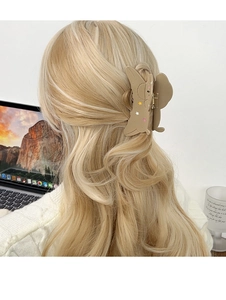 Detail of a large matte brown dog-shaped hair claw clip with colorful stars on wavy blonde hair