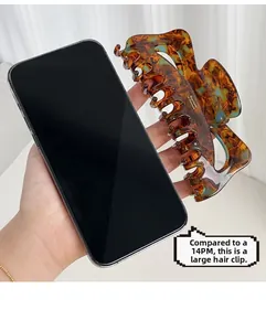 Large tortoiseshell hair claw size comparison with iPhone 14 Pro Max hand-held view