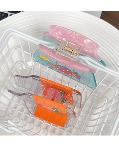 Détail de pinces à cheveux colorées en acétate avec ressort dans un panier blanc