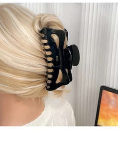 Detail of a large black glossy hair claw clip with golden lettering on blonde hair
