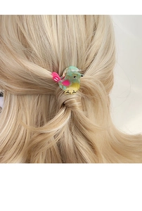 Macro detail of a colorful acetate bird hair clip worn on blonde hair showing material texture