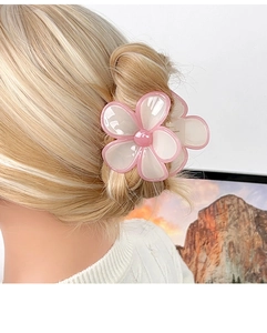 Dettaglio della grande pinza per capelli a fiore di frangipane rosa e bianco su capelli biondi
