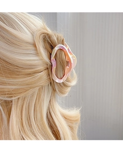 Detail showing gradient pink hair claw clip securing golden hair on textured grey background
