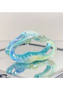 Macro view of iridescent blue and green hollow wave hair claw clip on mirror