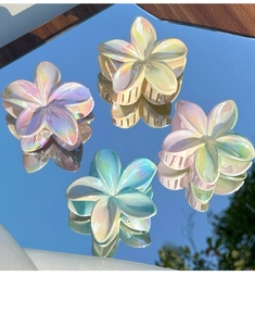 Macro detail of four pearlescent flower hair claws showing iridescent resin texture on mirrors