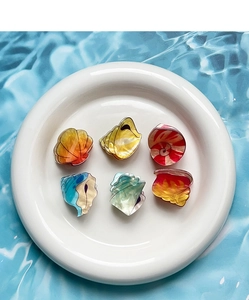 Detailed view of six colorful acrylic sea shell hair clips on a white ceramic plate
