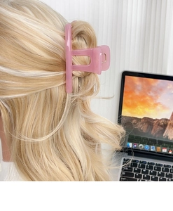 Pink translucent resin hair claw clip holding blonde wavy hair in a casual office setting