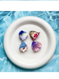 Set of four pearlescent ocean-themed hair clips in a white plate on a blue water background