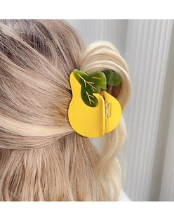 Close-up of a pear-shaped yellow acetate hair claw clip with green leaves on blonde hair