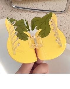 Detail of creative lemon-shaped hair claw clip with yellow finish and green leaves