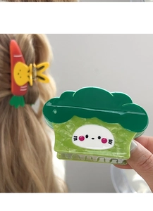 Detail of vegetable hair claws featuring green broccoli and carrot motifs with cute cat faces