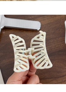 Detail of butterfly hair claw clip with pearlescent finish held by a hand over wood